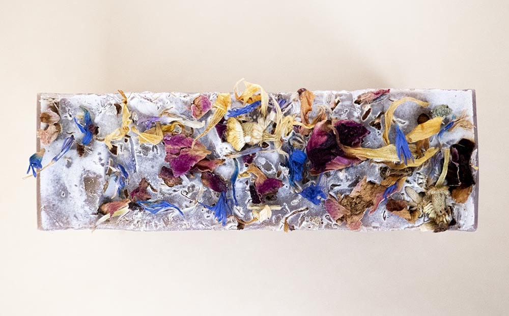 Top view of handcrafted bar of soap highlighting colorful dried flower details against a beige background