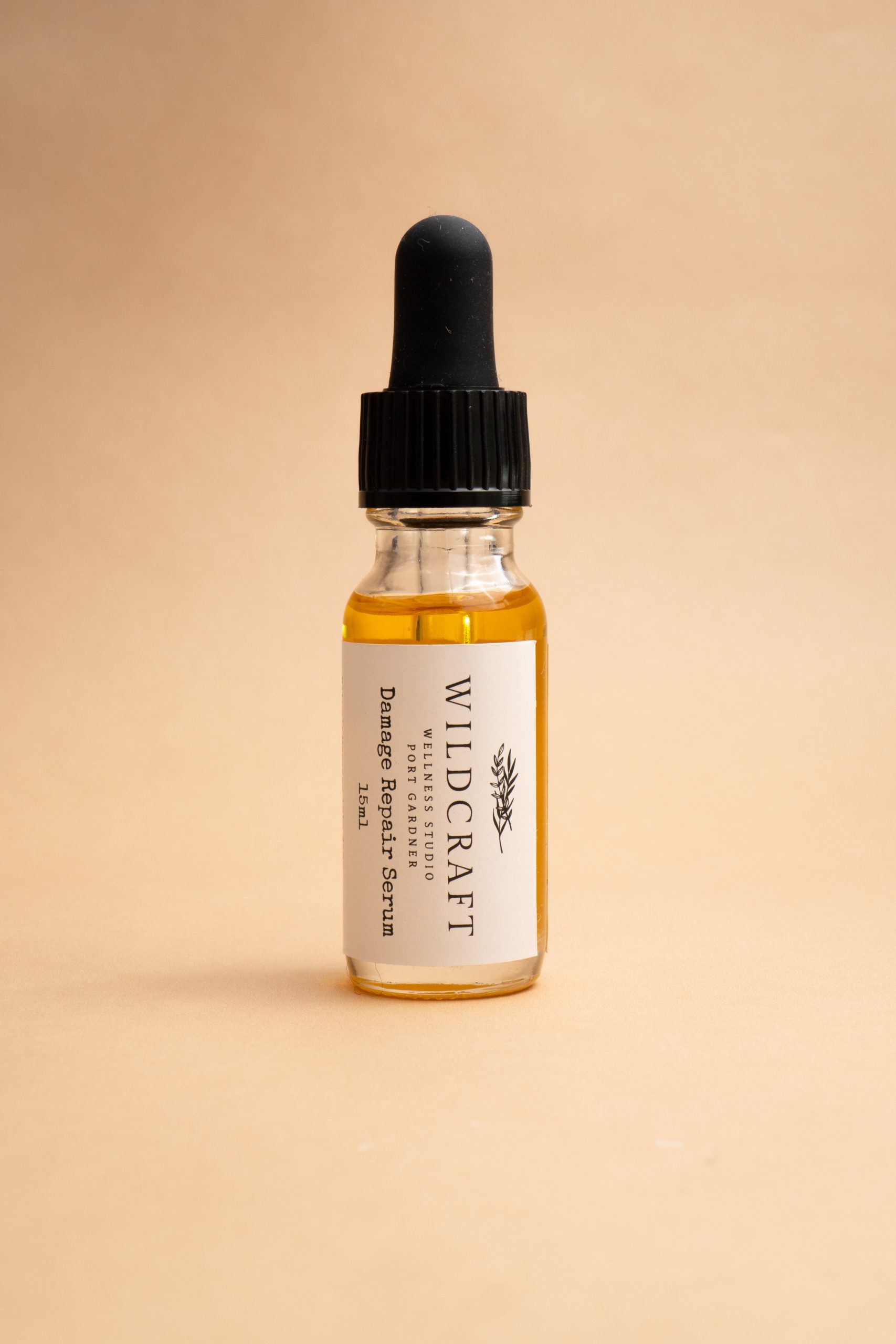 front angle phot of clear glass bottle of handmade damage repair serum against a clean beige background 