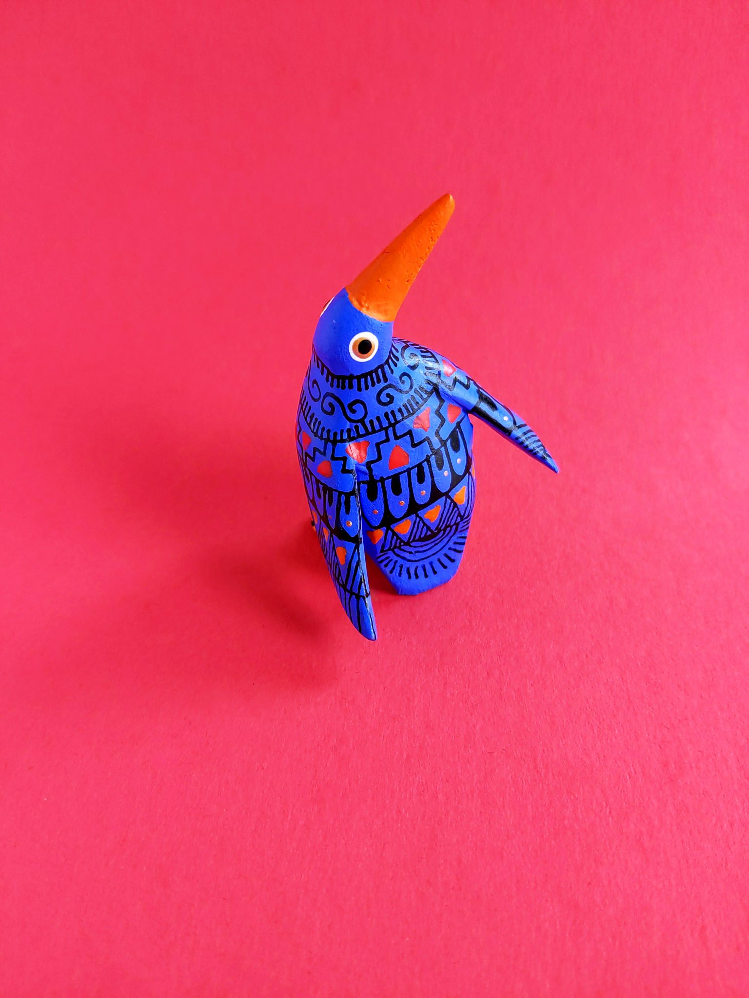 handcrafted small wooden bird with painted black, pink and orange detail against red plain background